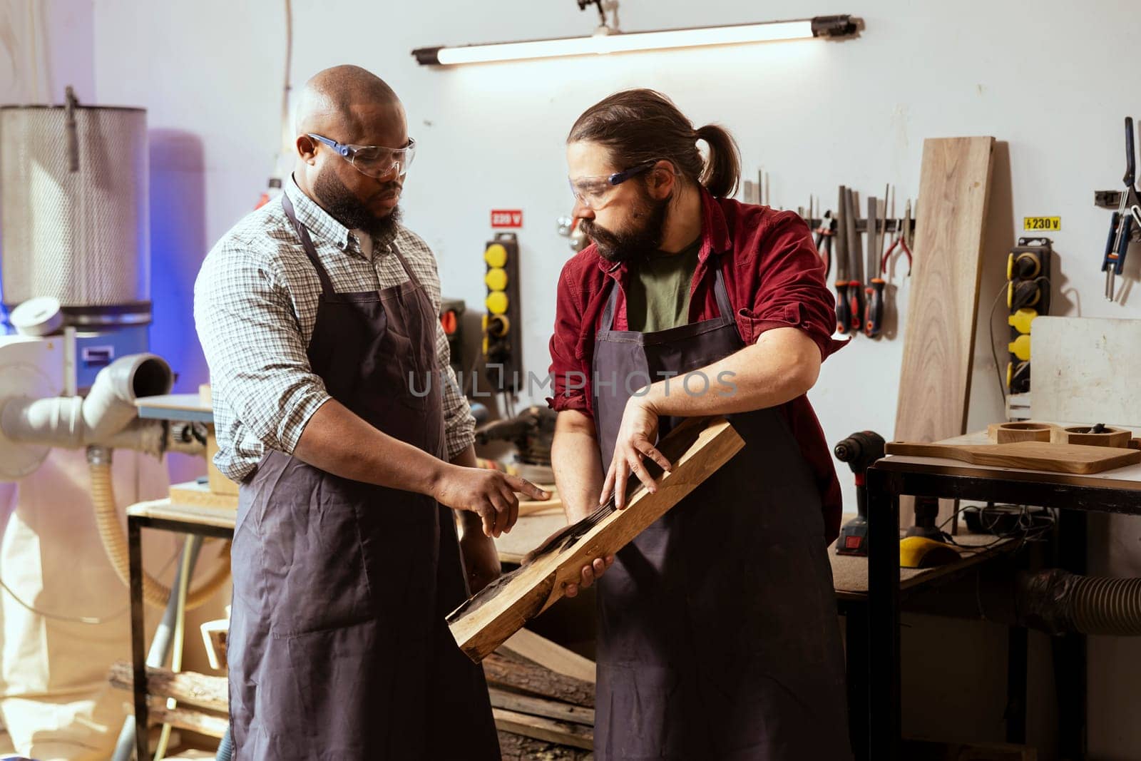 Carpenter holding timber block, brainstorming with coworker next steps in wood processing. Manufacturer in joinery and african american apprentice discussing what to do with piece of wood