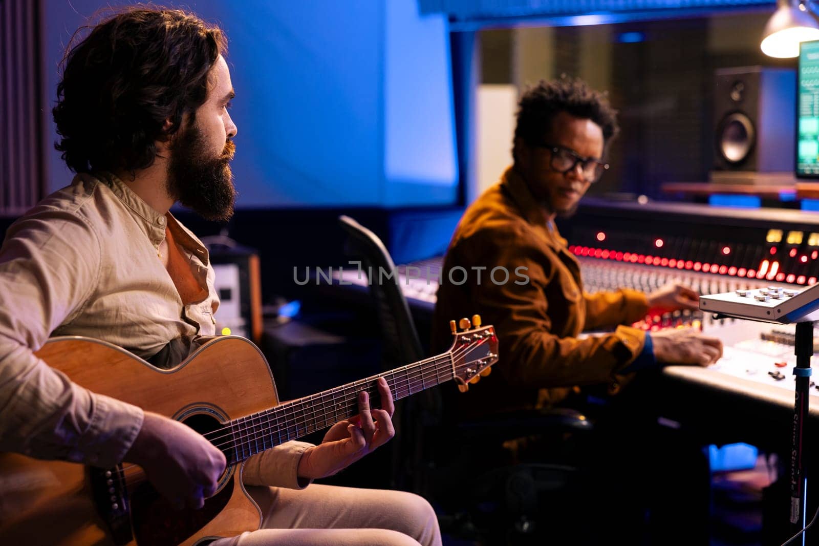 Young singer composer creating a new track on guitar in recording studio by DCStudio