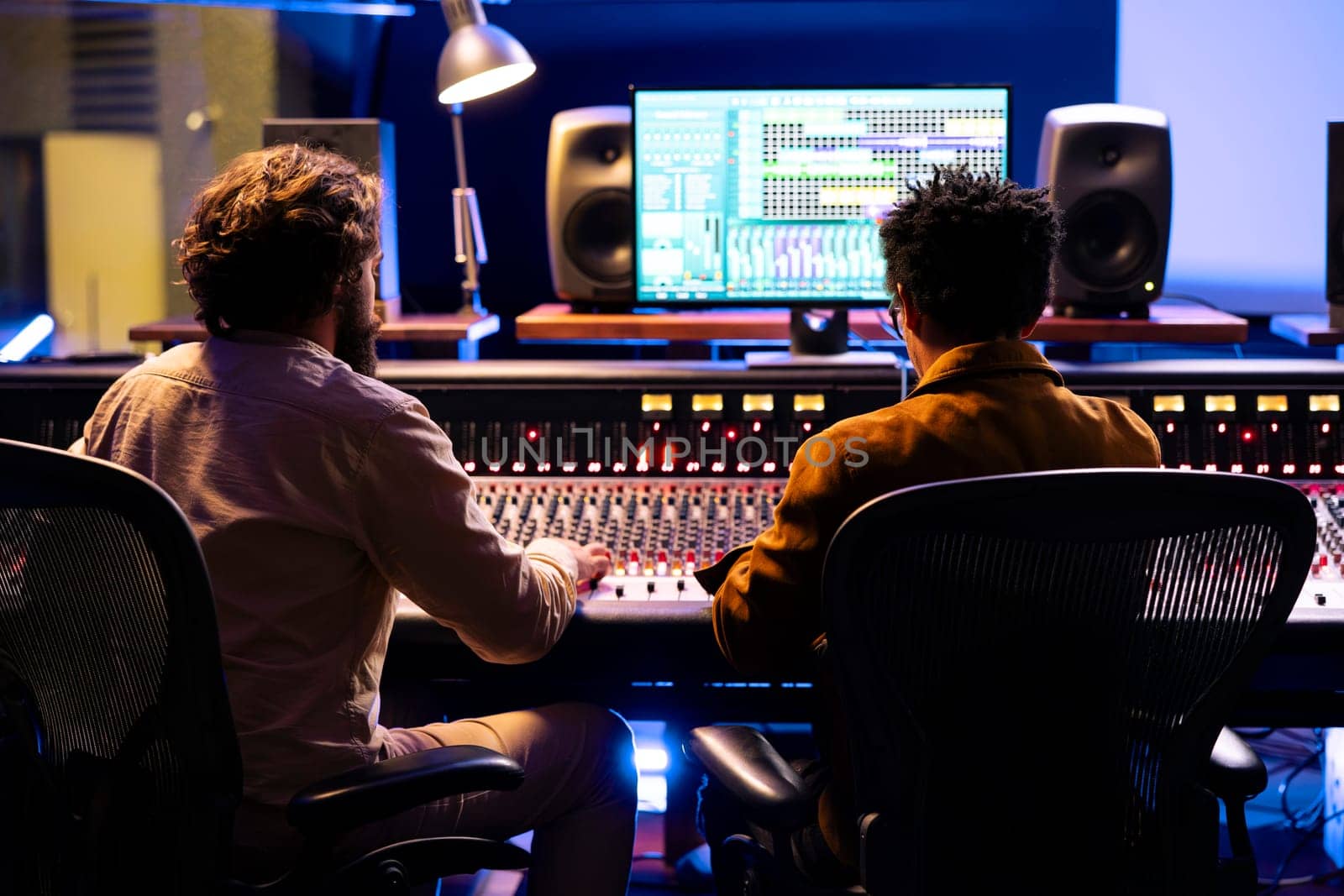 Singer and producer working together in professional music studio, collaborating on a hit song in control room. Audio engineer editing records with mixing and mastering techniques.
