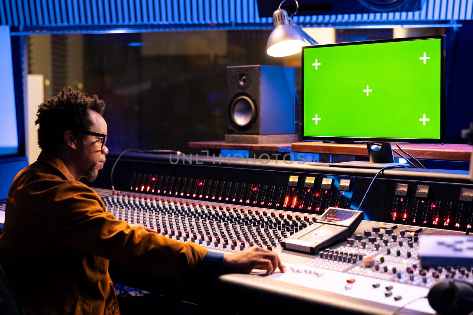 Sound designer operating mixing console and greenscreen monitor, twisting various knobs and buttons in professional studio. Audio technician editing tracks in post production, technical gear.