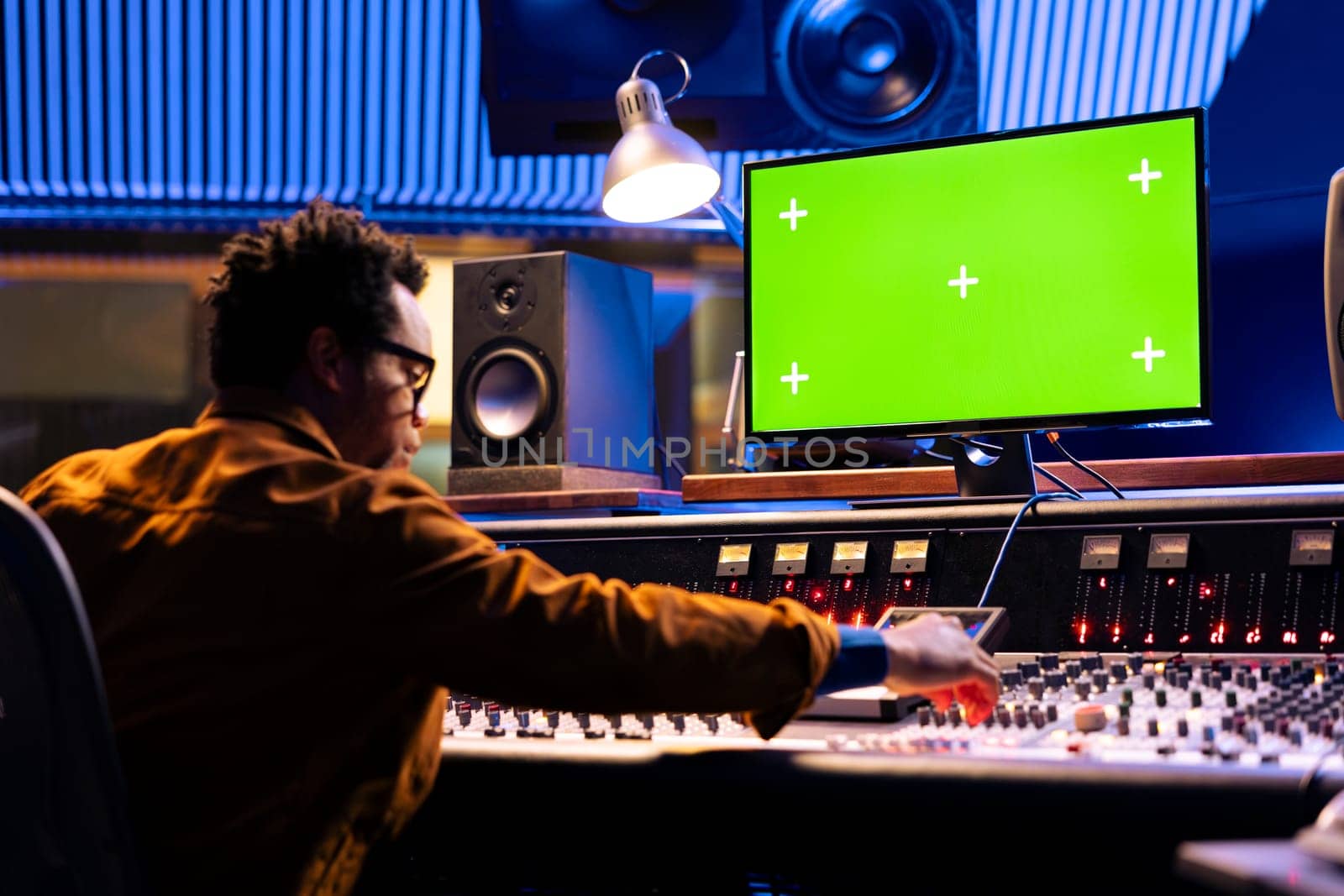 African american producer editing music on console with isolated display pc, mixing and mastering sounds on control desk board. Young audio engineer operates on sliders and buttons.