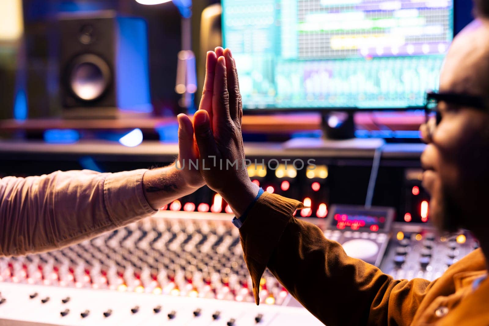 Pleased artist doing high five gesture with sound designer after finishing a song, processing and editing music for his new album. Singer and producer celebrating successful tracks in studio.