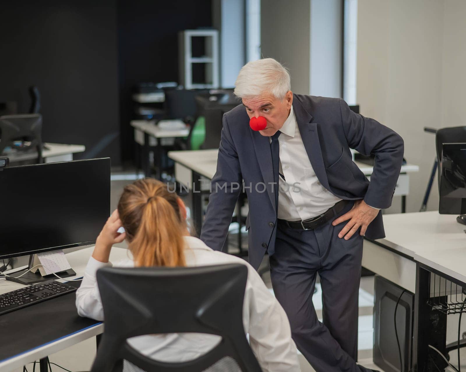 Elderly Caucasian man wearing a clown nose swears at his subordinate in the office. by mrwed54