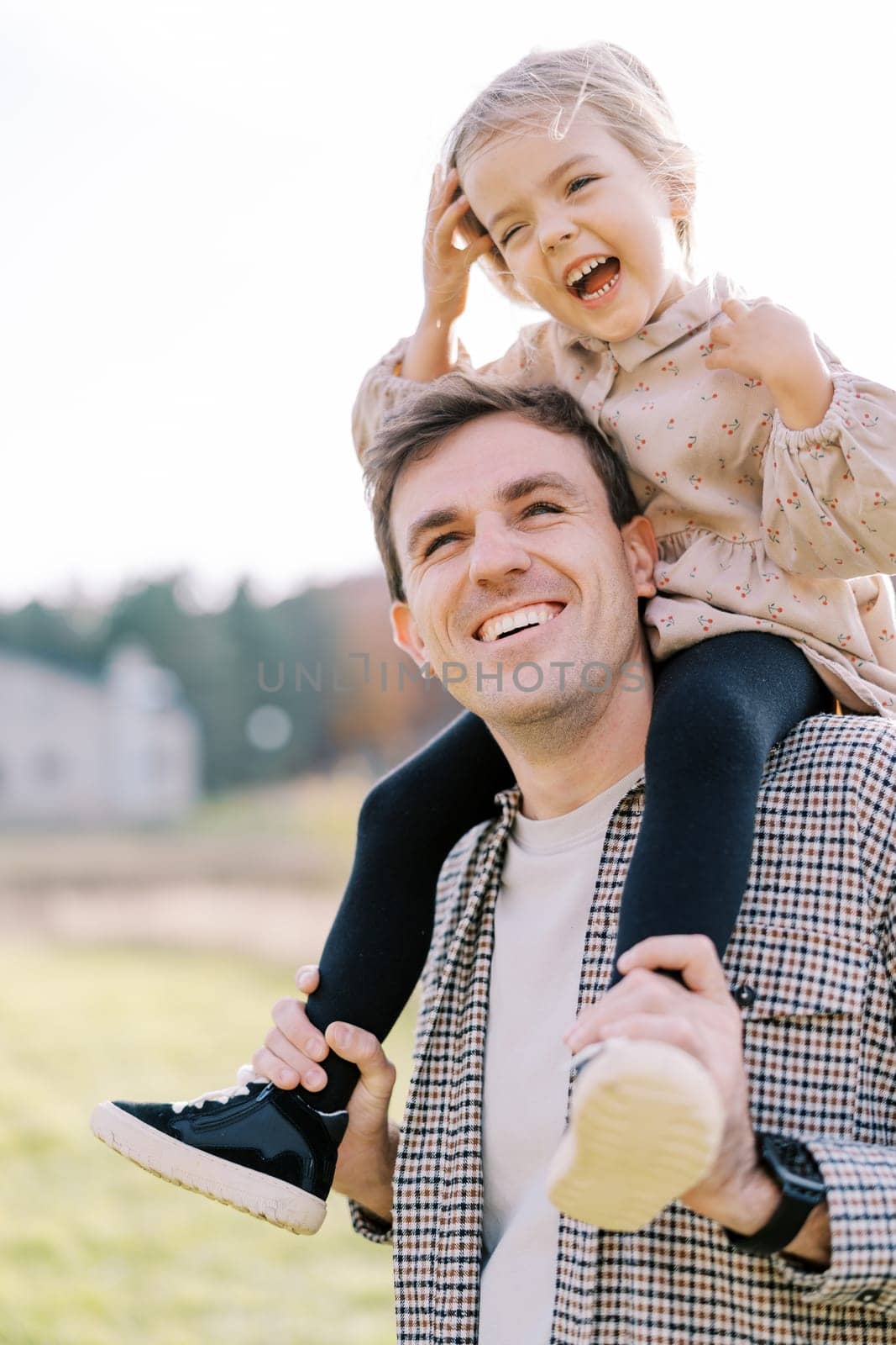 Little laughing girl straightens her hair while sitting on the shoulders of a smiling dad. High quality photo