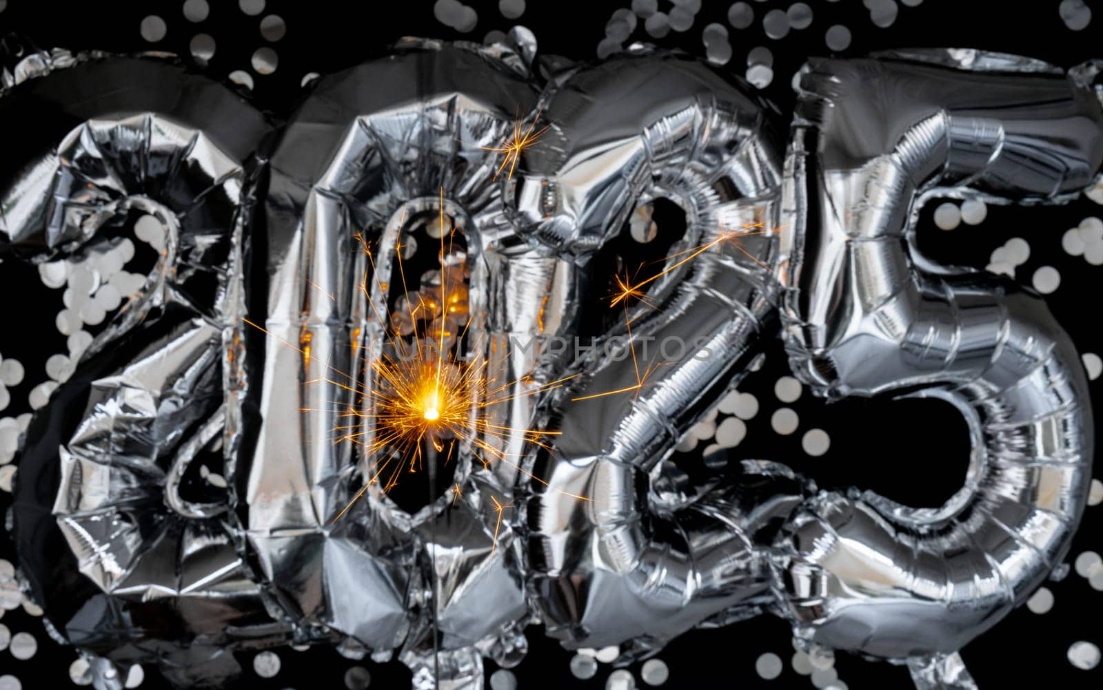 Happy new year 2025 metallic balloons with confetti and sparkler firework Bengal lights on dark black background. Greeting card silver foil balloons numbers Christmas holiday concept. Celebration party congratulation decoration