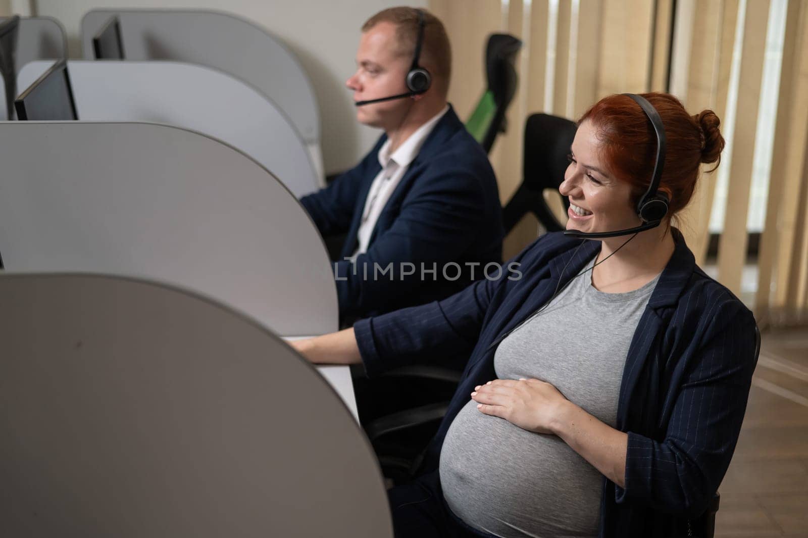 Two friendly call center employees serve customers. Man and pregnant woman talking on a headset in the office