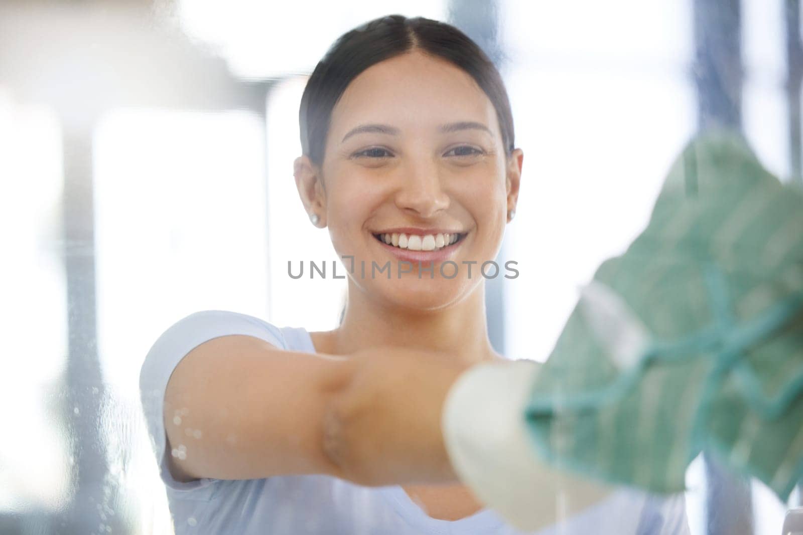 Happy woman, housekeeping and cleaning window with cloth for disinfection, hygiene or health and safety at home. Female person, domestic or young maid with smile for glass surface or cleaner service by YuriArcurs