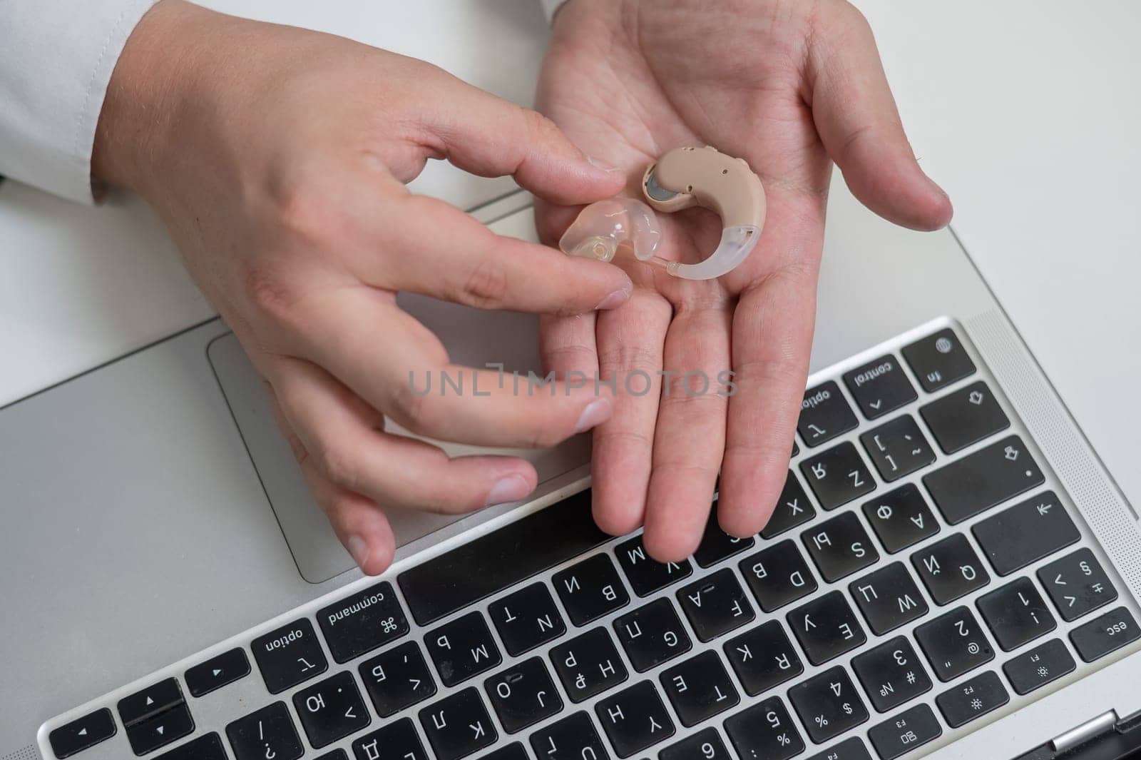 Close-up of a man's hands with a hearing aid near a laptop