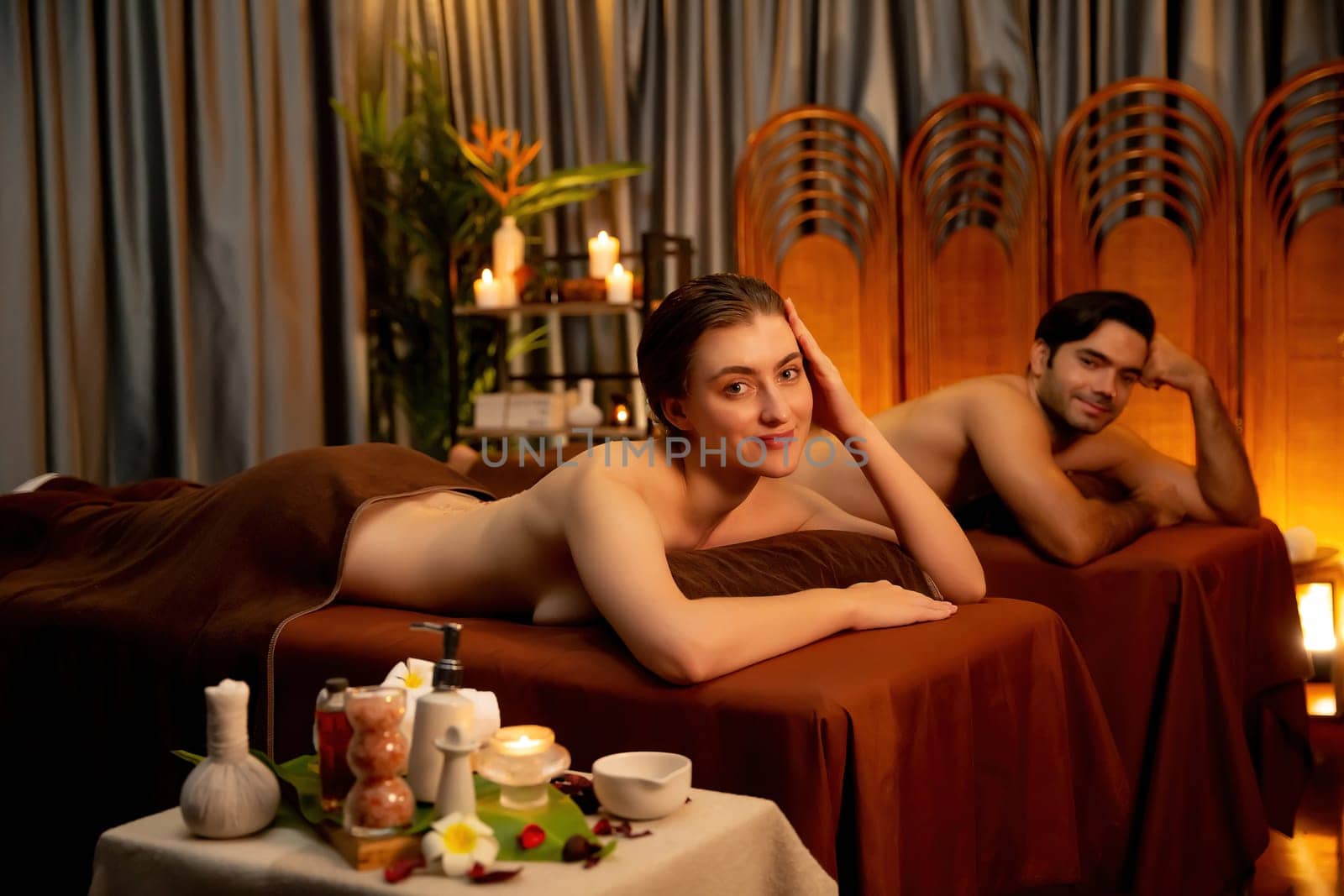 Couple customer having exfoliation treatment in luxury spa salon with warmth candle light ambient. Salt scrub beauty treatment in Health spa body scrub. Quiescent