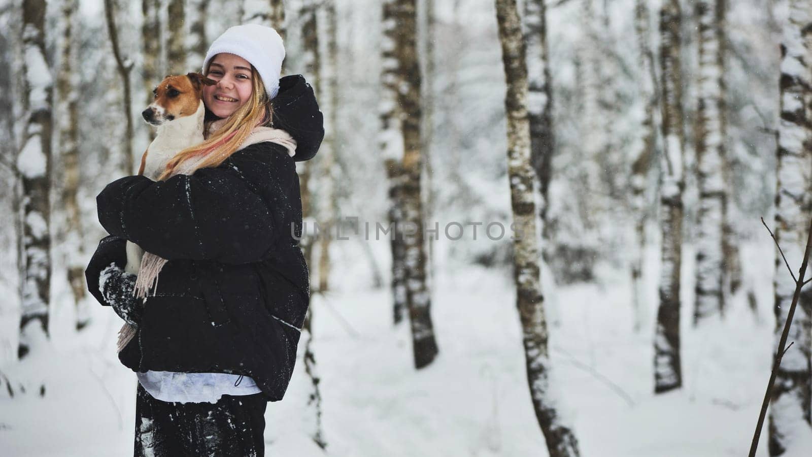 A girl cuddles a Jack Russell Terrier dog in the woods in winter. by DovidPro