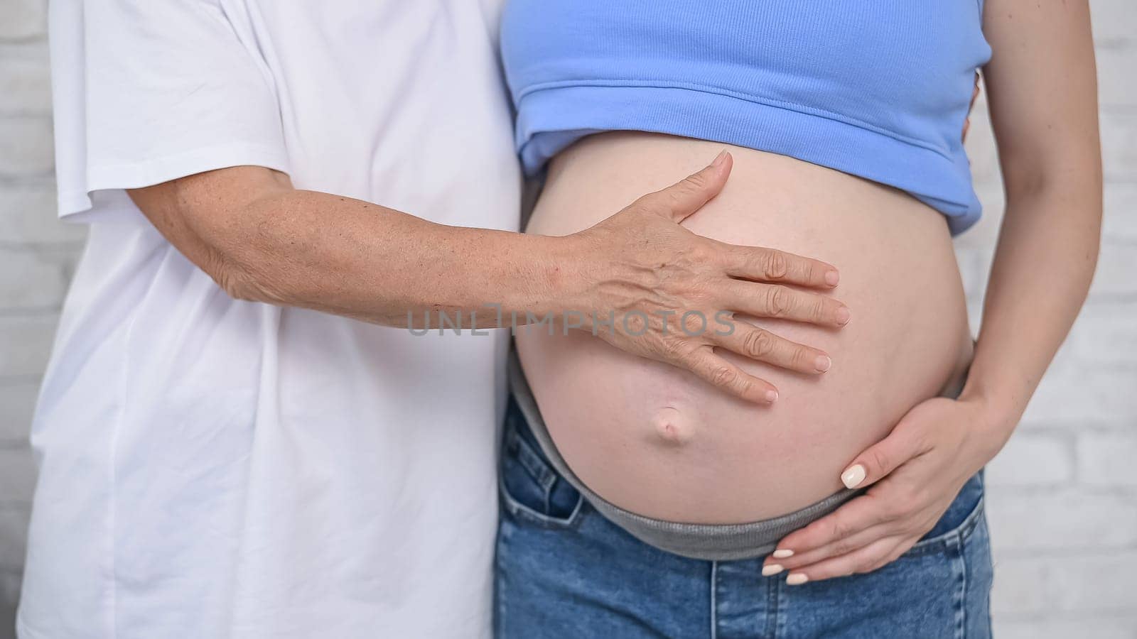 An elderly woman touches the belly of her pregnant daughter. Close-up. by mrwed54