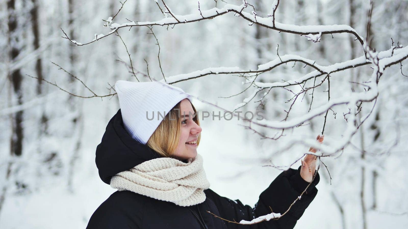 A girl gently touches snowy tree branches in the forest. by DovidPro