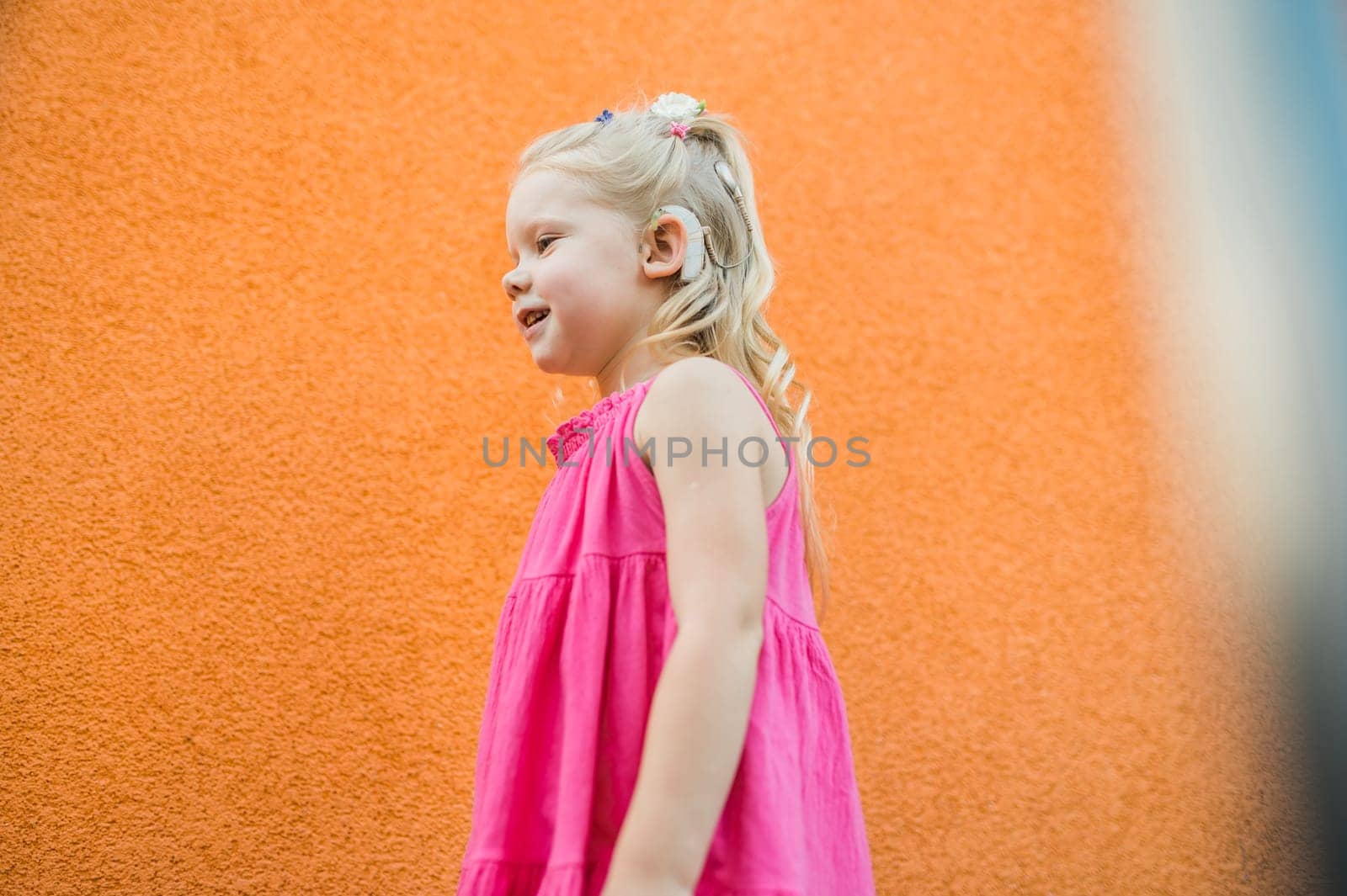 Child girl walks and have fun outdoor with cochlear implant on the head. Hearing aid and treatment concept. Inclusion and disability. by Satura86