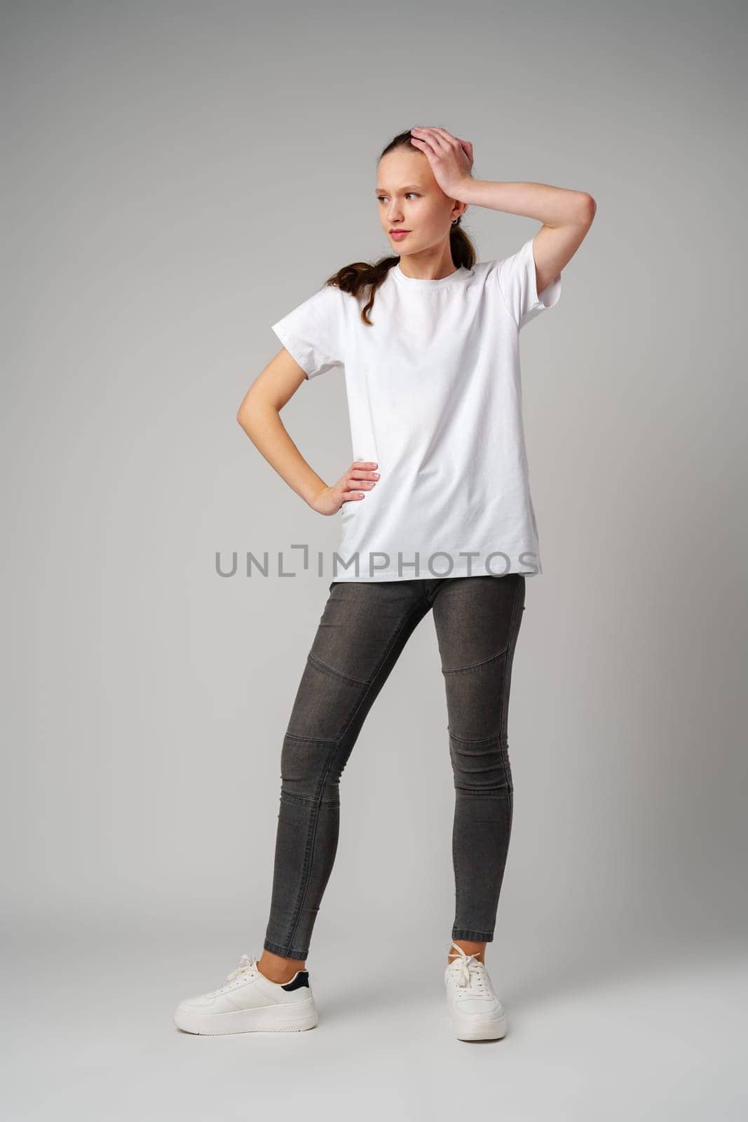 Beautiful young girl posing in white T-shirt and jeans on gray background in studio