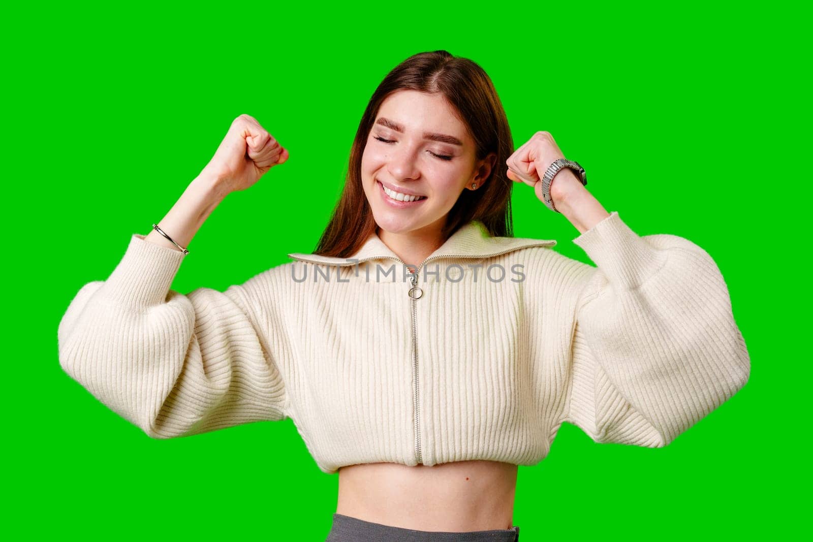 A woman wearing a white sweater is showcasing her strength by flexing her arm muscles. She appears confident and determined, highlighting her physical fitness and dedication to exercise.