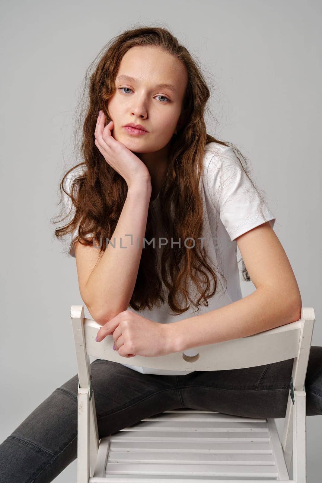 Curly girl model posing on a chair against gray background in studio