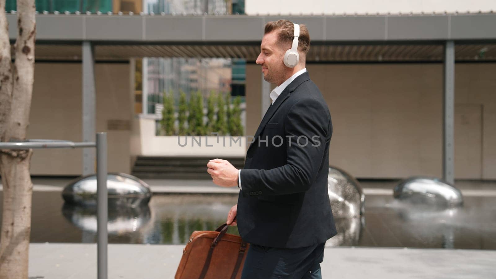 Happy project manager with headphone walking workplace while moving to relaxed music. side view of smart caucasian businessman going to meeting while dancing and walking along the city street. Urbane.