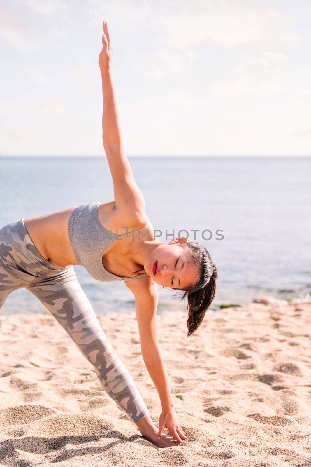 young asian woman in sportswear stretching on the beach with yoga poses, concept of mental relaxation and healthy lifestyle, copy space for text