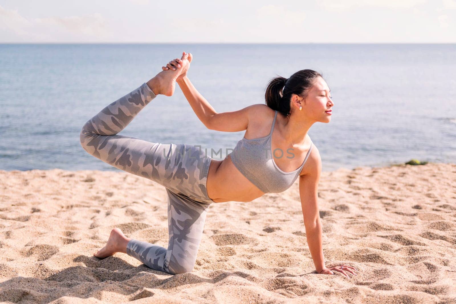 young asian woman in sportswear stretching on the beach with yoga poses, concept of mental relaxation and healthy lifestyle