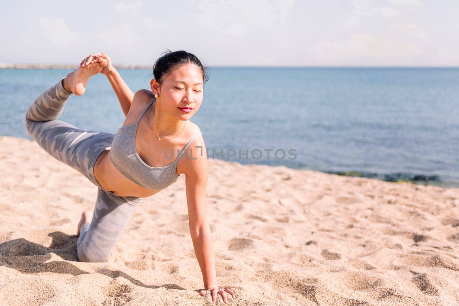 young asian woman in sportswear stretching on the beach with yoga poses, concept of mental relaxation and healthy lifestyle, copy space for text