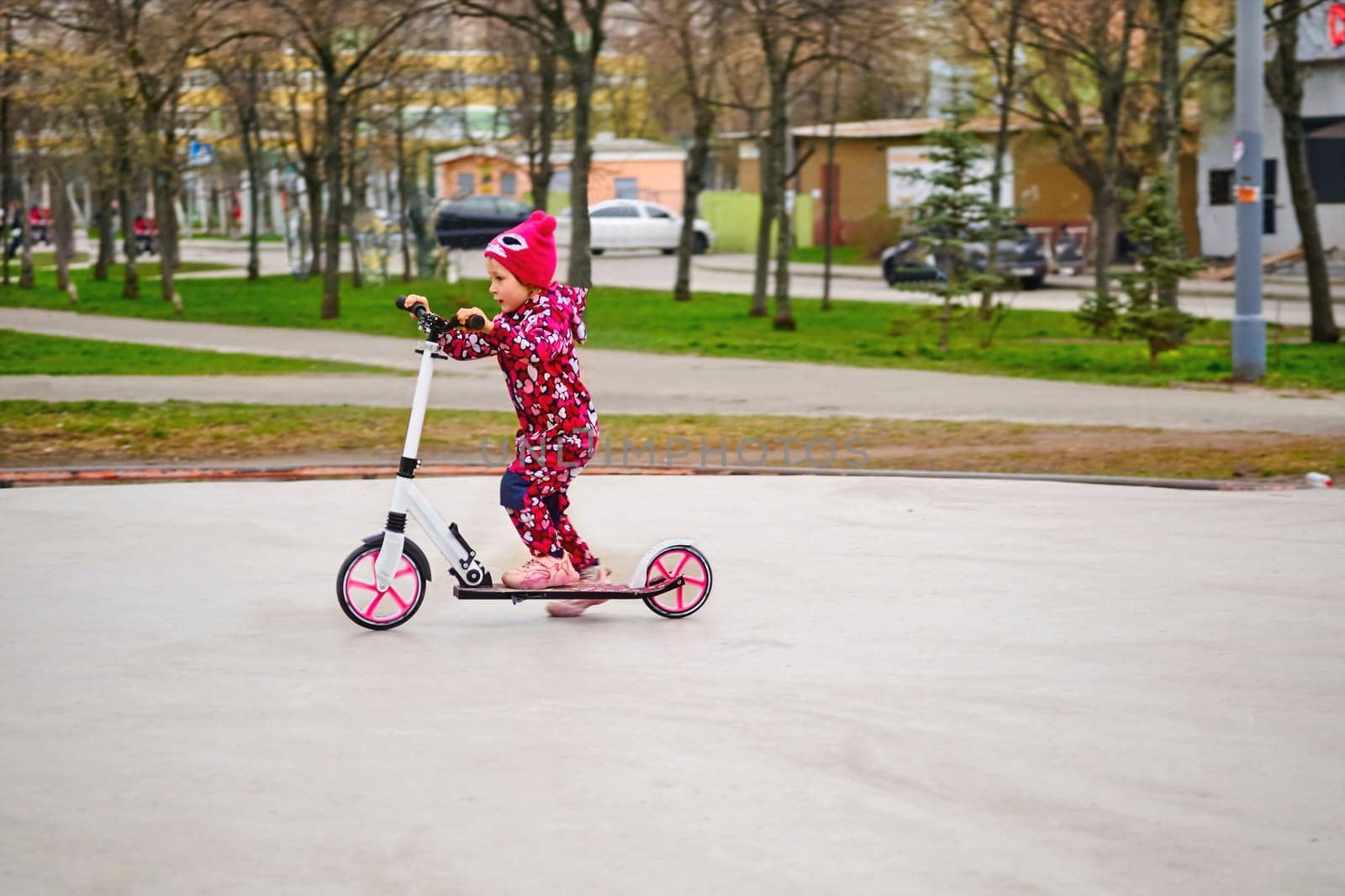 Joyful active child rides a pink scooter in a city park by jovani68