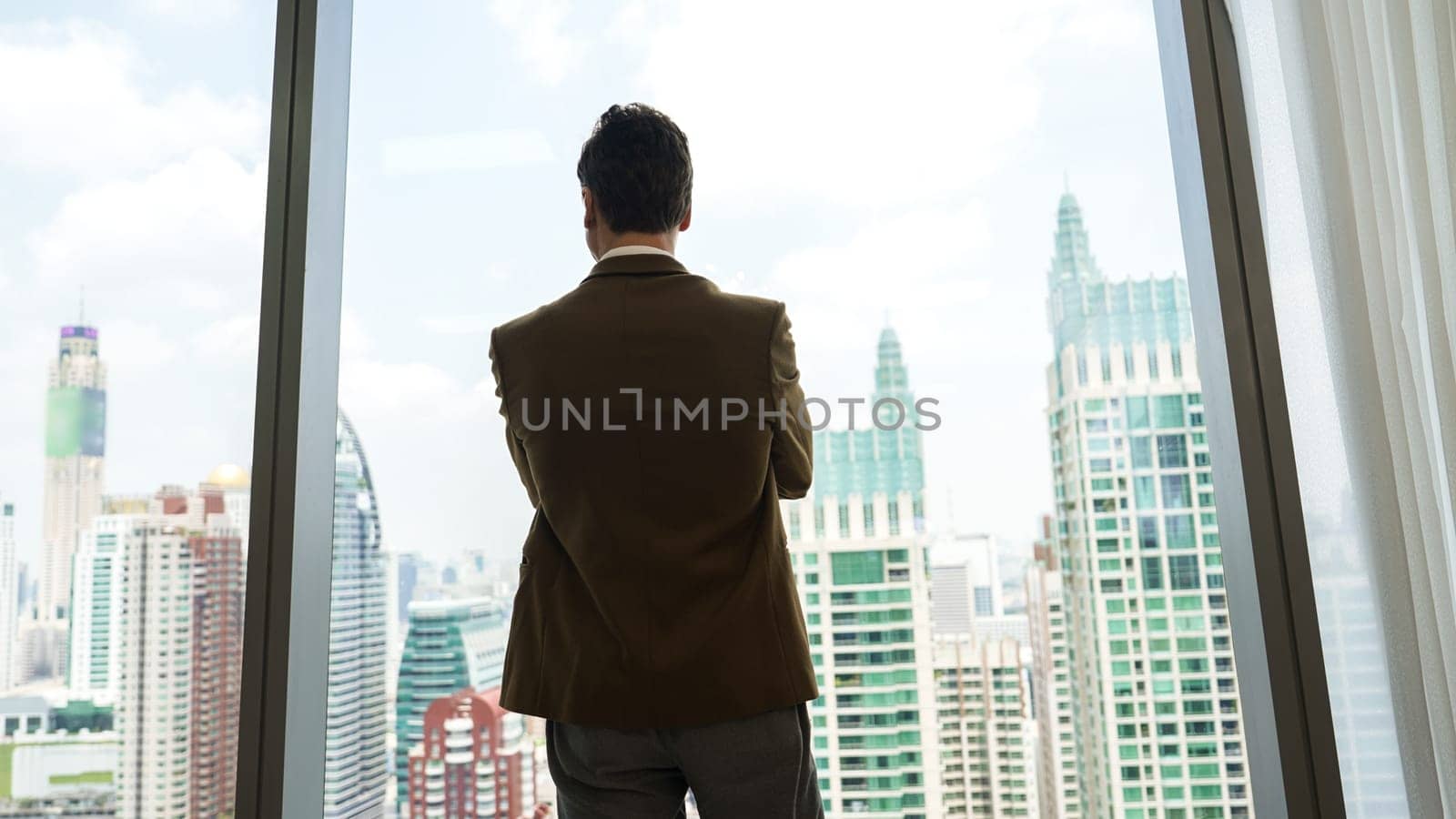 Back view ambitious businessman standing in ornamented office gazing out window to cityscape skyline. Determination and business ambition drive business career toward to bright future