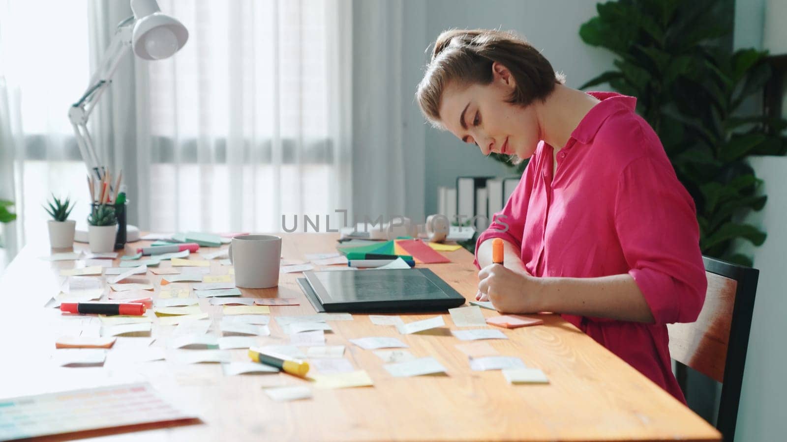 Top view of designer writing idea on colorful sticky notes while sitting at meeting table with tablet display logo design. Professional business woman looking design and making a decision. Symposium.