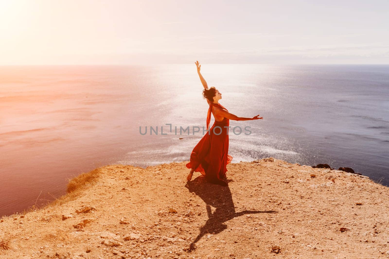 Woman red dress sea. Female dancer in a long red dress posing on a beach with rocks on sunny day. Girl on the nature on blue sky background. by Matiunina