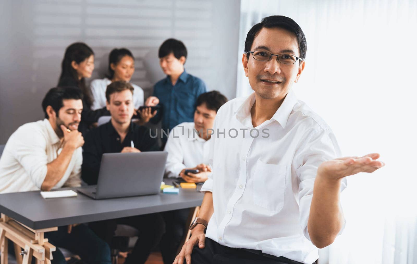 Confidence and happy smiling businessman portrait making advertising posture with background of business team working in office. Office worker and positive workplace for job recruitment. Prudent
