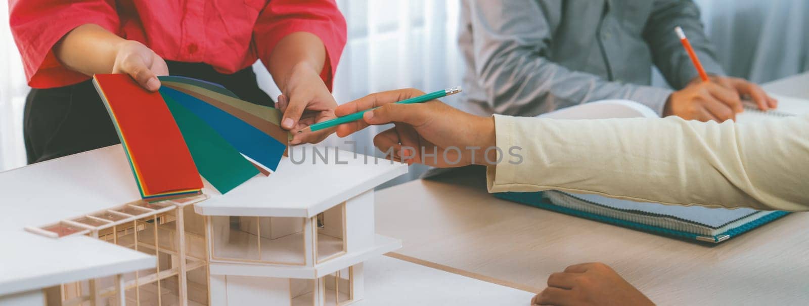 Cropped image of skilled architect and interior designer team collaborate to select house color theme at meeting room with house model placed on table. Creative working and design concept. Variegated.