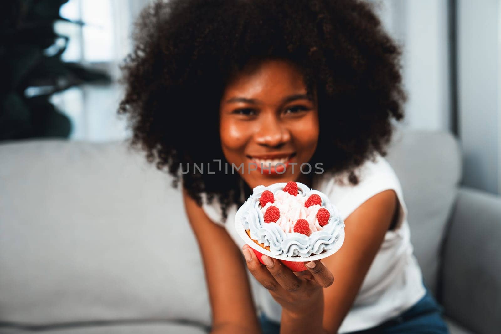 Beautiful young African blogger presenting cupcake with selective focus in concept special cuisine. Content creating of social media online with favorite sweets bakery dish. Tastemaker.
