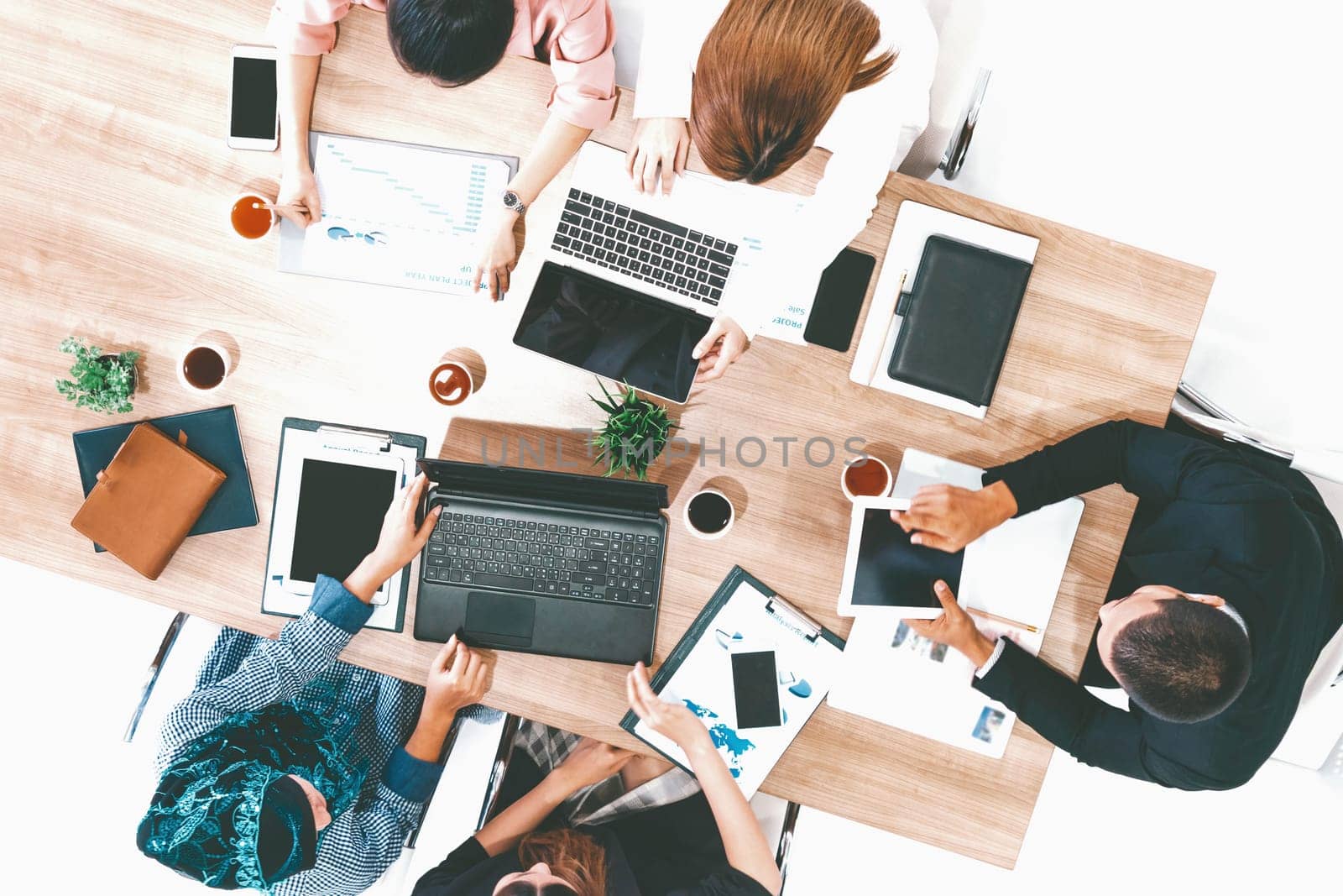 Top view of businessman executive in group meeting with other businessmen and businesswomen in modern office with laptop computer, coffee and document on table. People corporate business team uds
