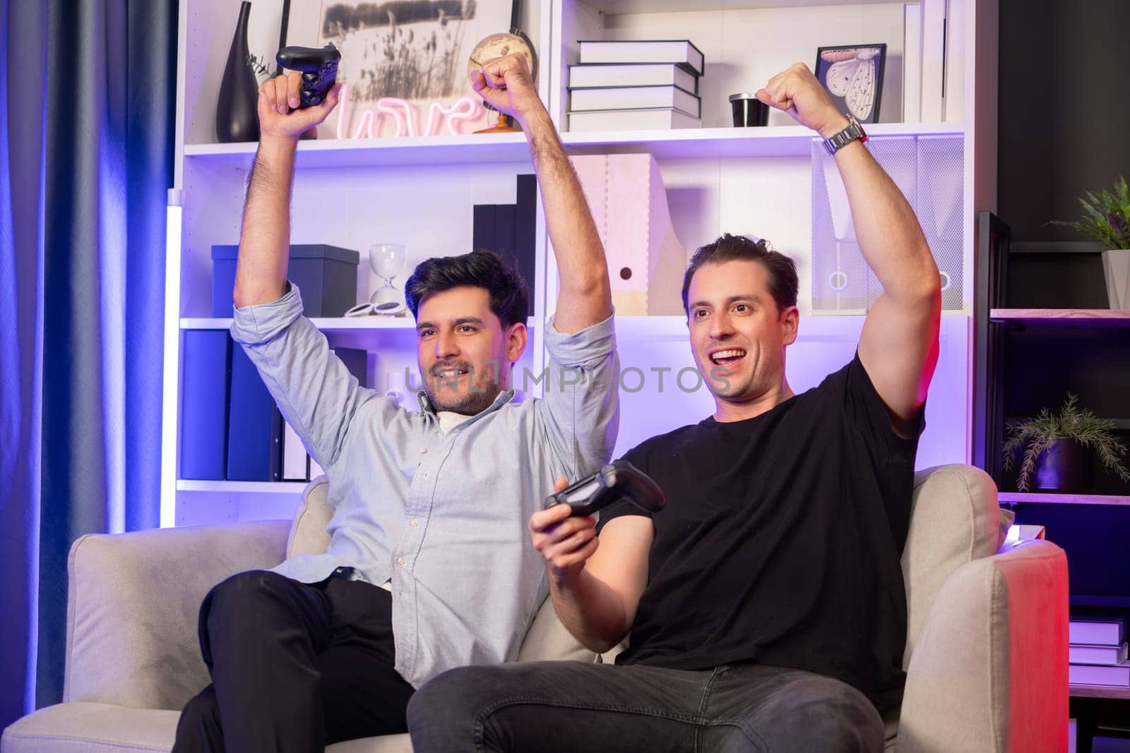 Winner and loser players of buddy friend gamers playing video game on TV using joysticks in studio room with neon blue light. Comfy living indoor at home place with cheerful fighting winner. Sellable.
