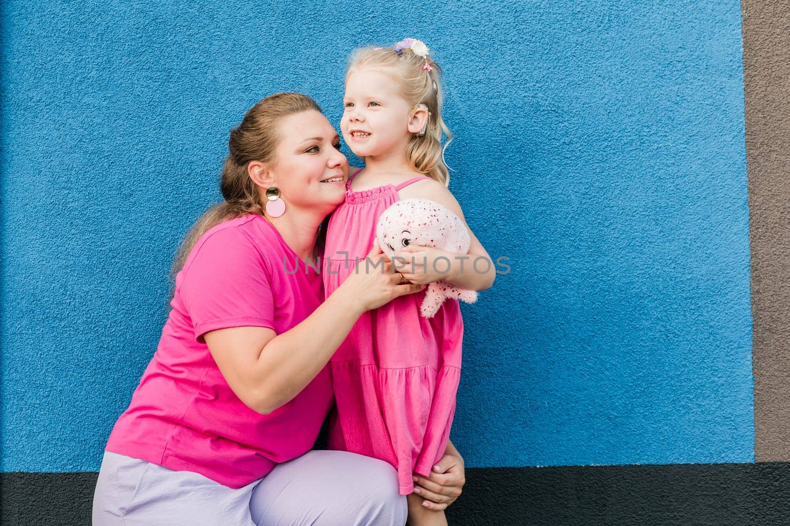 Deaf child with cochlear implant for hearing audio and aid for impairment having fun and laughs with mother outdoor in summer. Sound fitting device to help with communication listening and interaction.