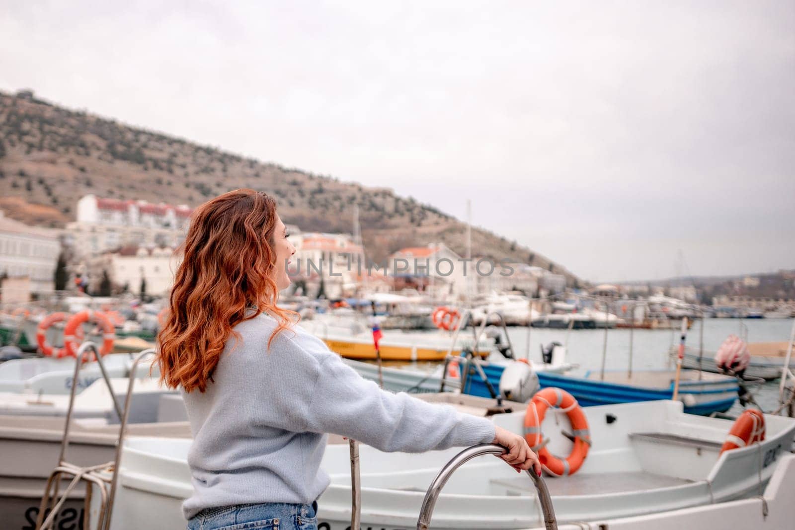 A woman stands in front of a row of boats, some of which have orange life preservers on them. The scene is peaceful and serene, with the boats and the woman creating a sense of calmness and relaxation