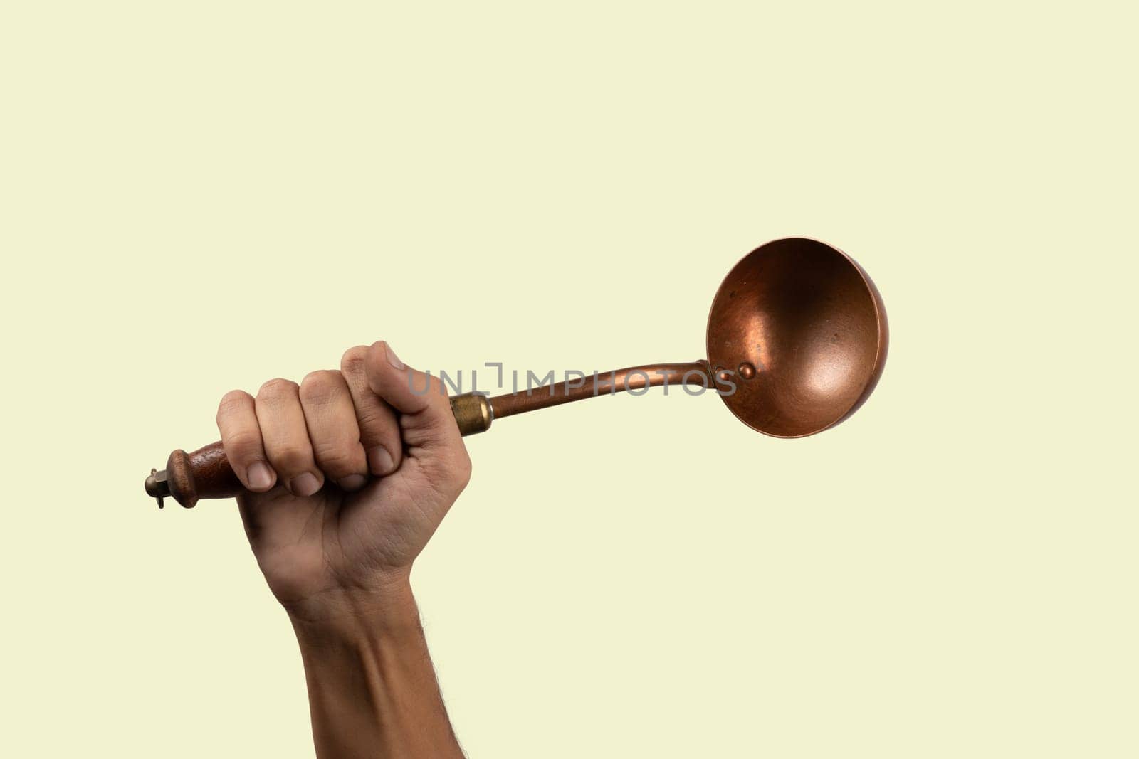 Black male hand holding a brass vintage kitchen ladle isolated green background. High quality photo