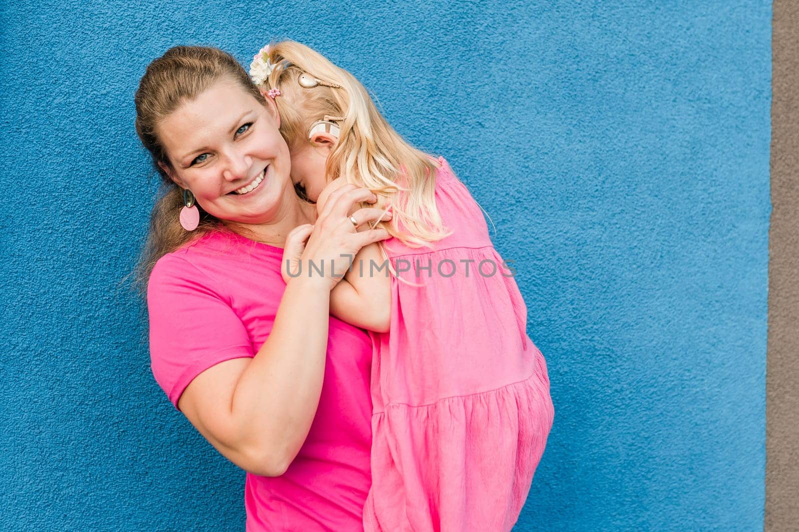 Blonde little girl with cochlear implant playing with her mother outdoor. Hear impairment deaf and health concept. Diversity and inclusion. Copy space.