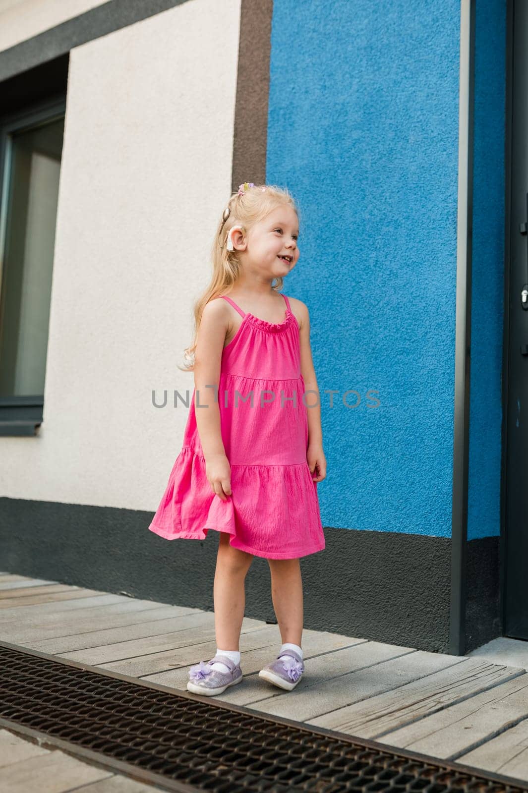 Child girl walks and have fun outdoor with cochlear implant on the head. Hearing aid and treatment concept. Copy space vertical.