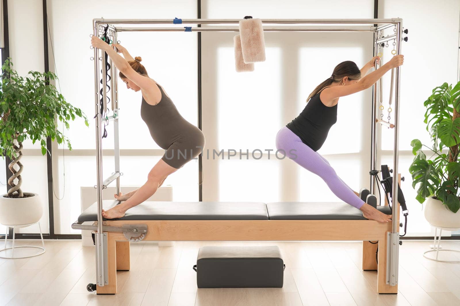 Two pregnant women are doing Pilates on a Cadillac reformer