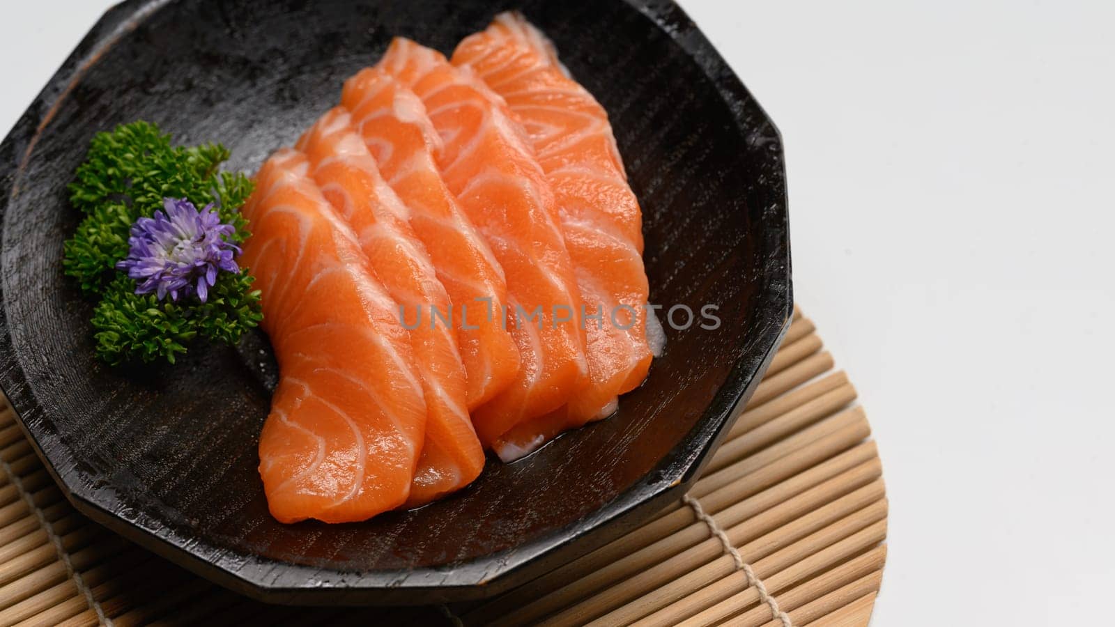 Delicious sashimi salmon arranged on a black stone plate with parsley leave.