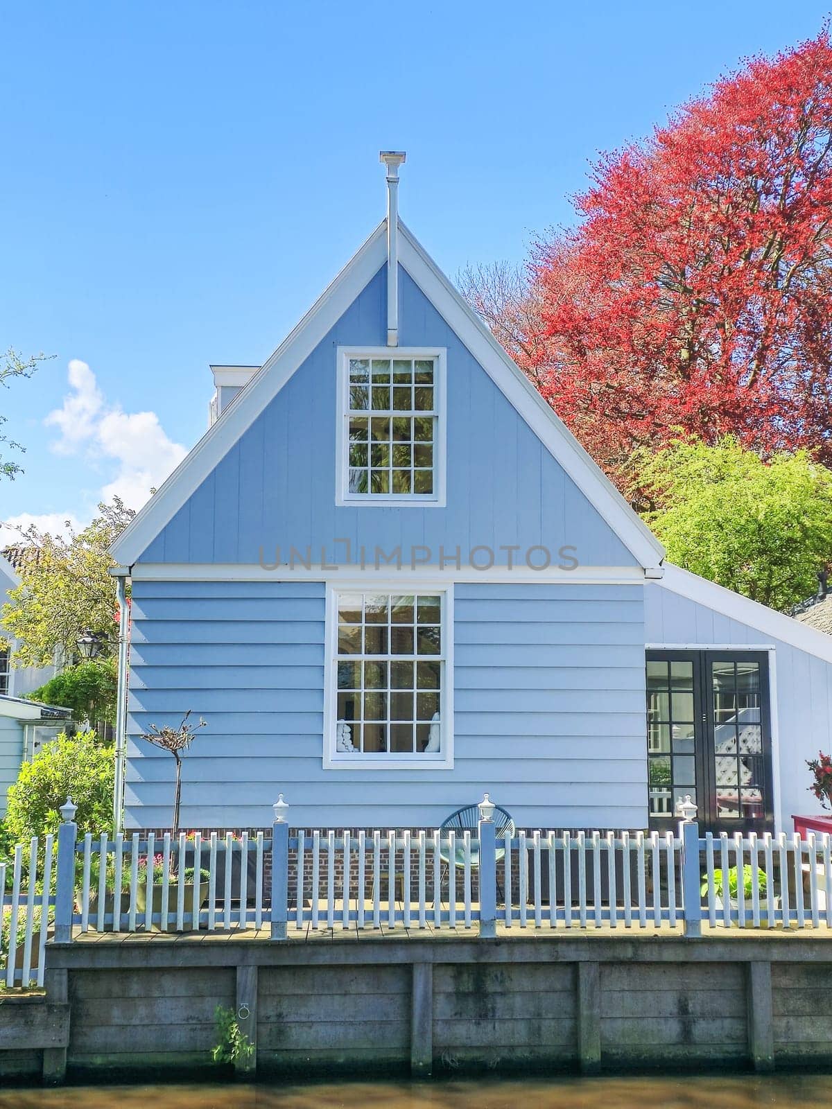 A charming blue house with a white picket fence nestled in a serene environment, exuding a sense of tranquility and nostalgia by fokkebok