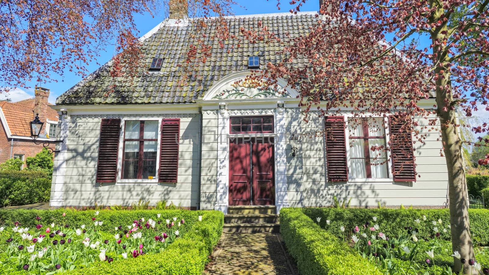 A charming white house adorned with vibrant red shutters and a inviting red door, standing out against a backdrop of greenery by fokkebok