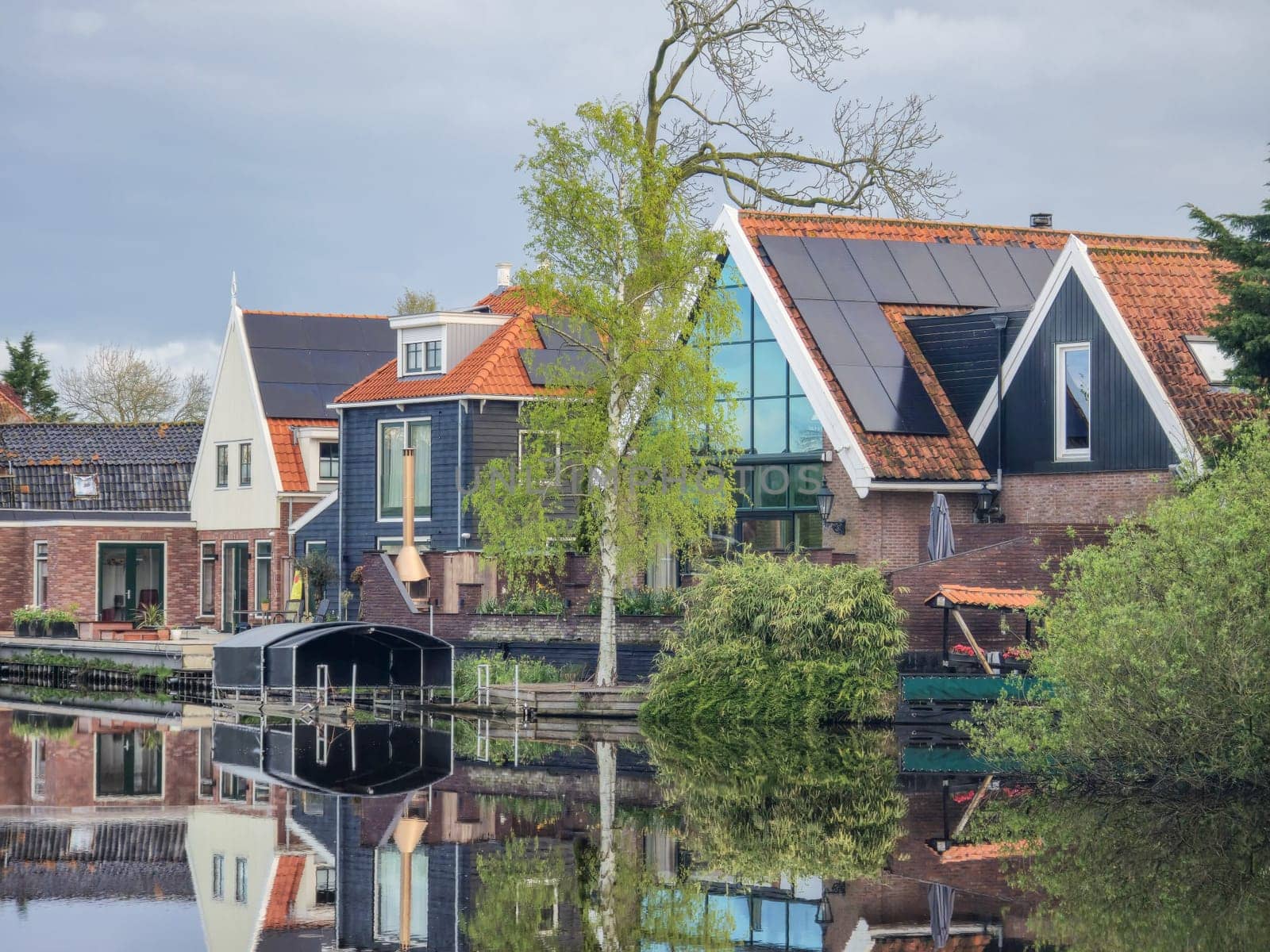 A picturesque scene of a charming row of houses lined up next to a peaceful body of water, creating a tranquil and idyllic setting by fokkebok