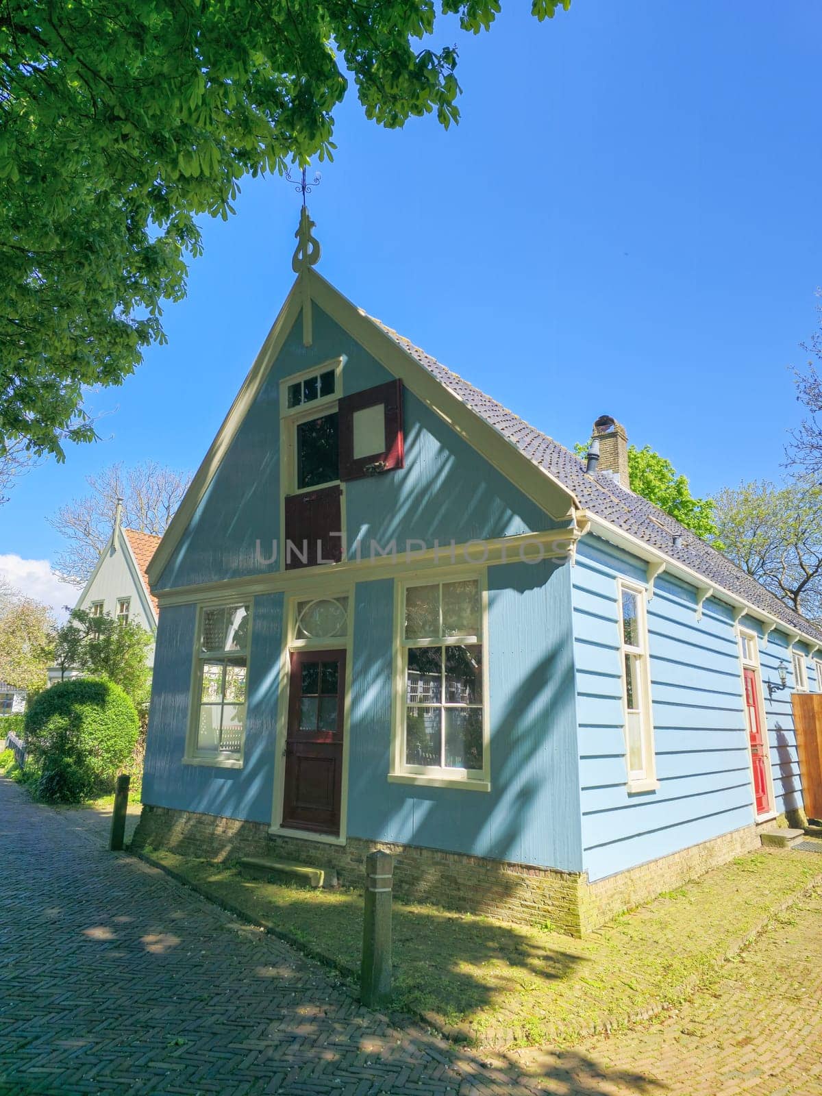 A charming small blue house stands out with its vibrant red door, creating a picturesque scene in a quaint setting by fokkebok