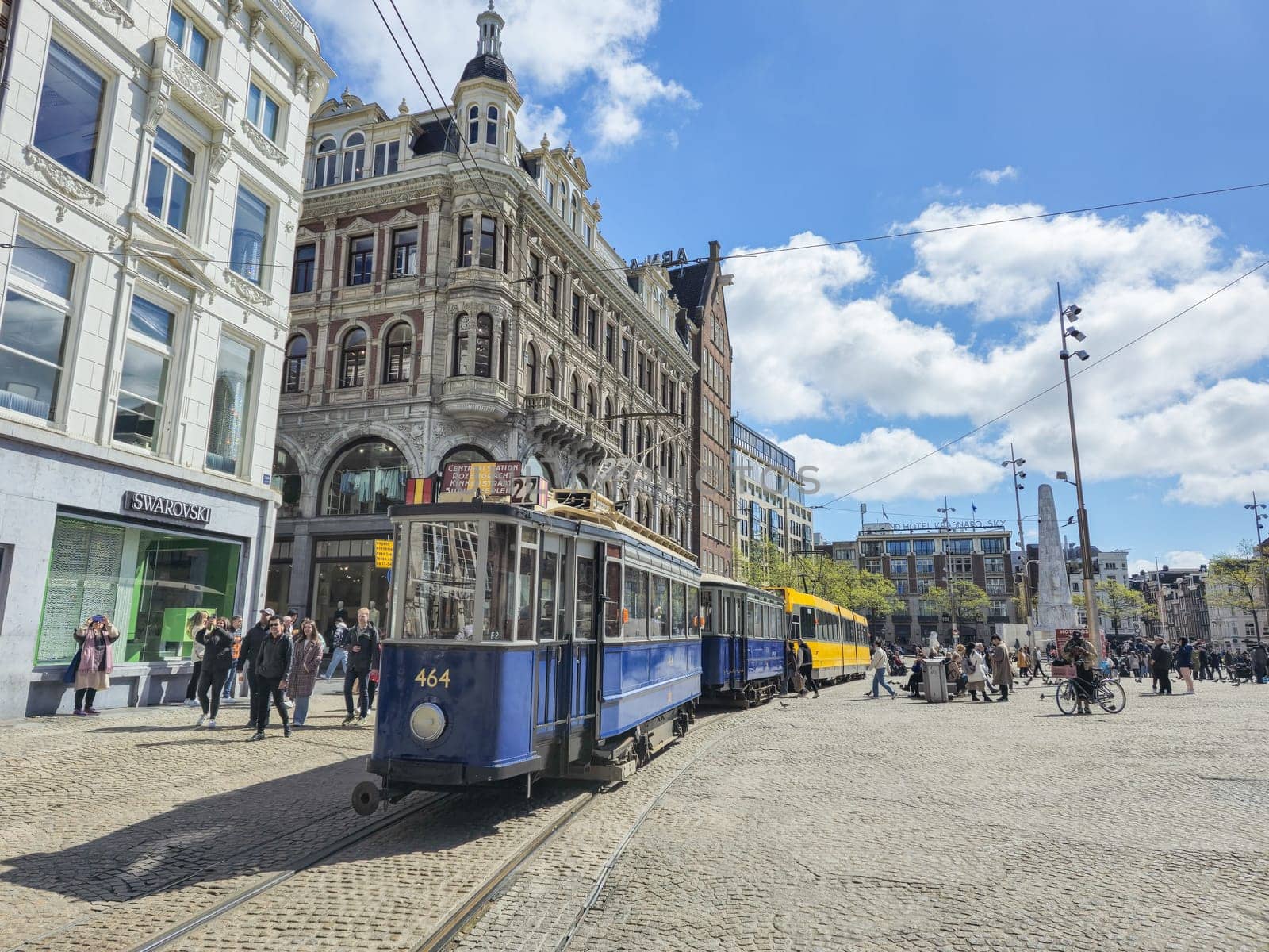 A vibrant blue and yellow trolley travels along a bustling city street, adding a splash of color to the urban landscape by fokkebok