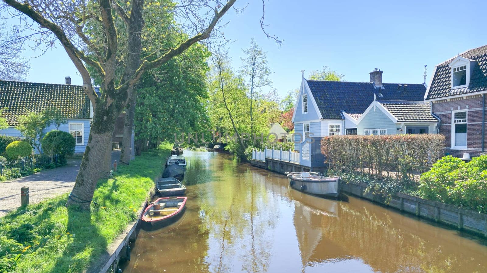 Boats leisurely glide through the calm canal lined with charming houses on a tranquil day. Broek in Waterland Netherlands