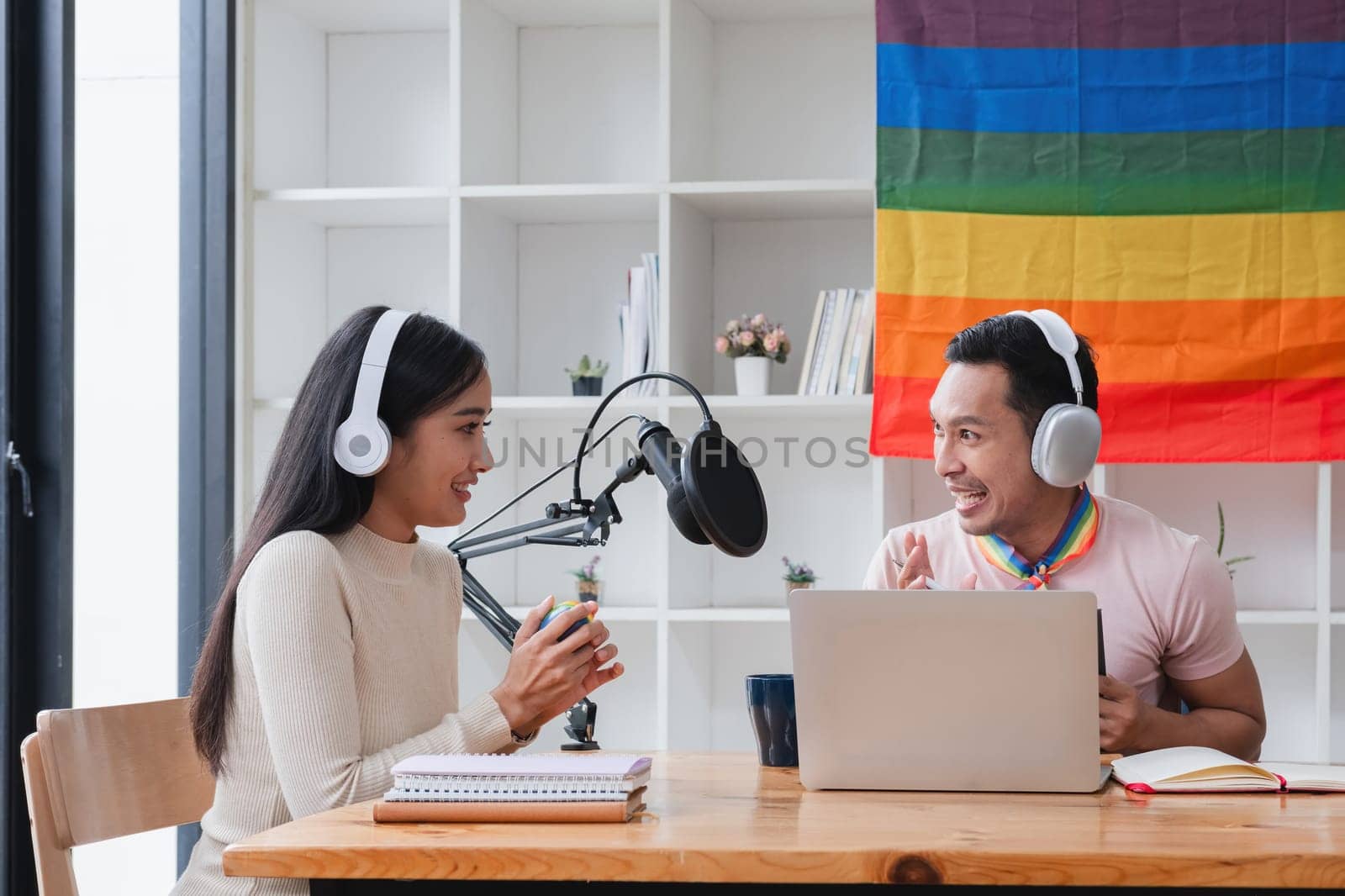 A young gay man and his girlfriend use a laptop and microphone to stream podcast audio at a studio talking about gender liberation..