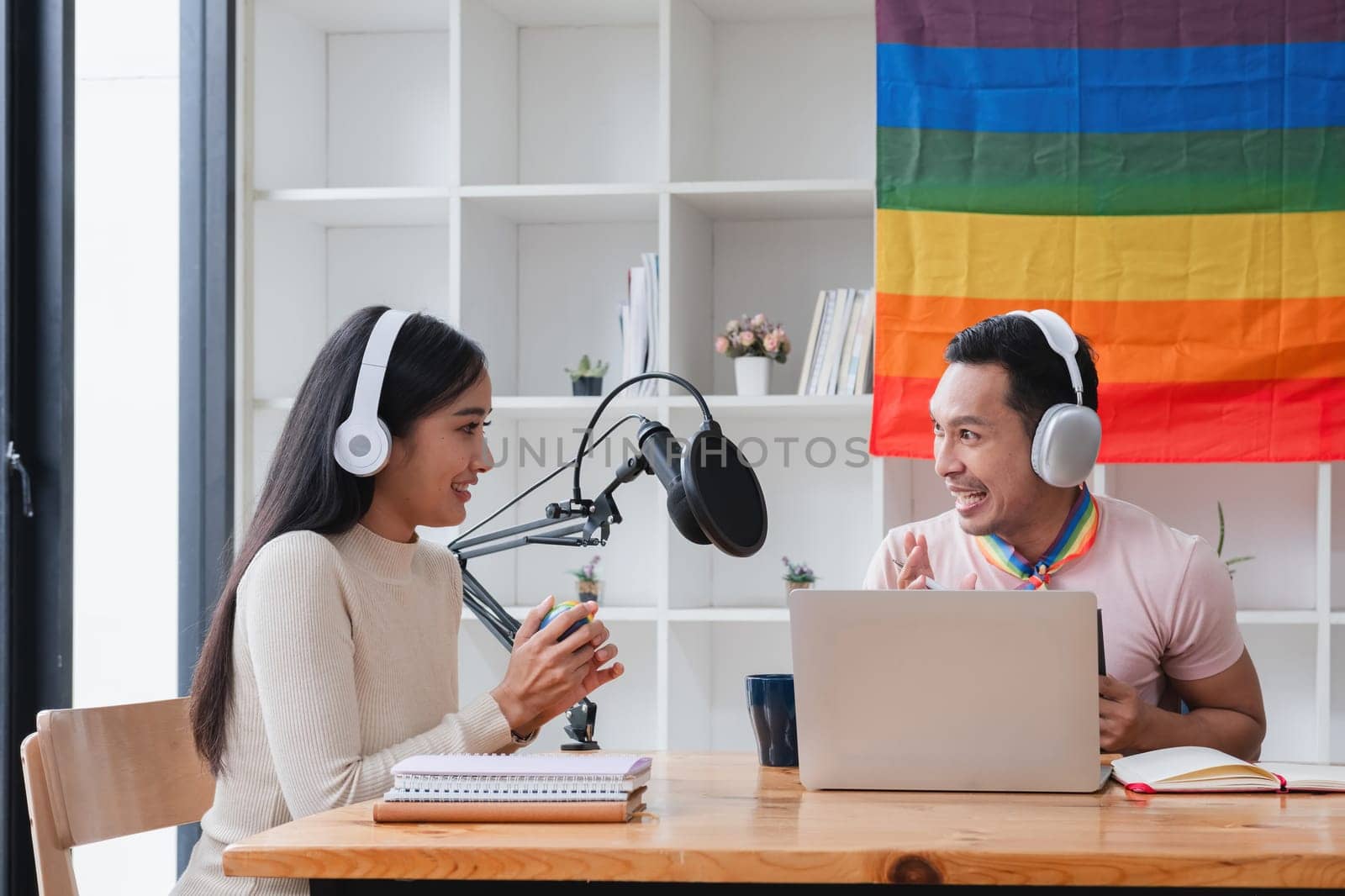 A young gay man and his girlfriend use a laptop and microphone to stream podcast audio at a studio talking about gender liberation. by wichayada