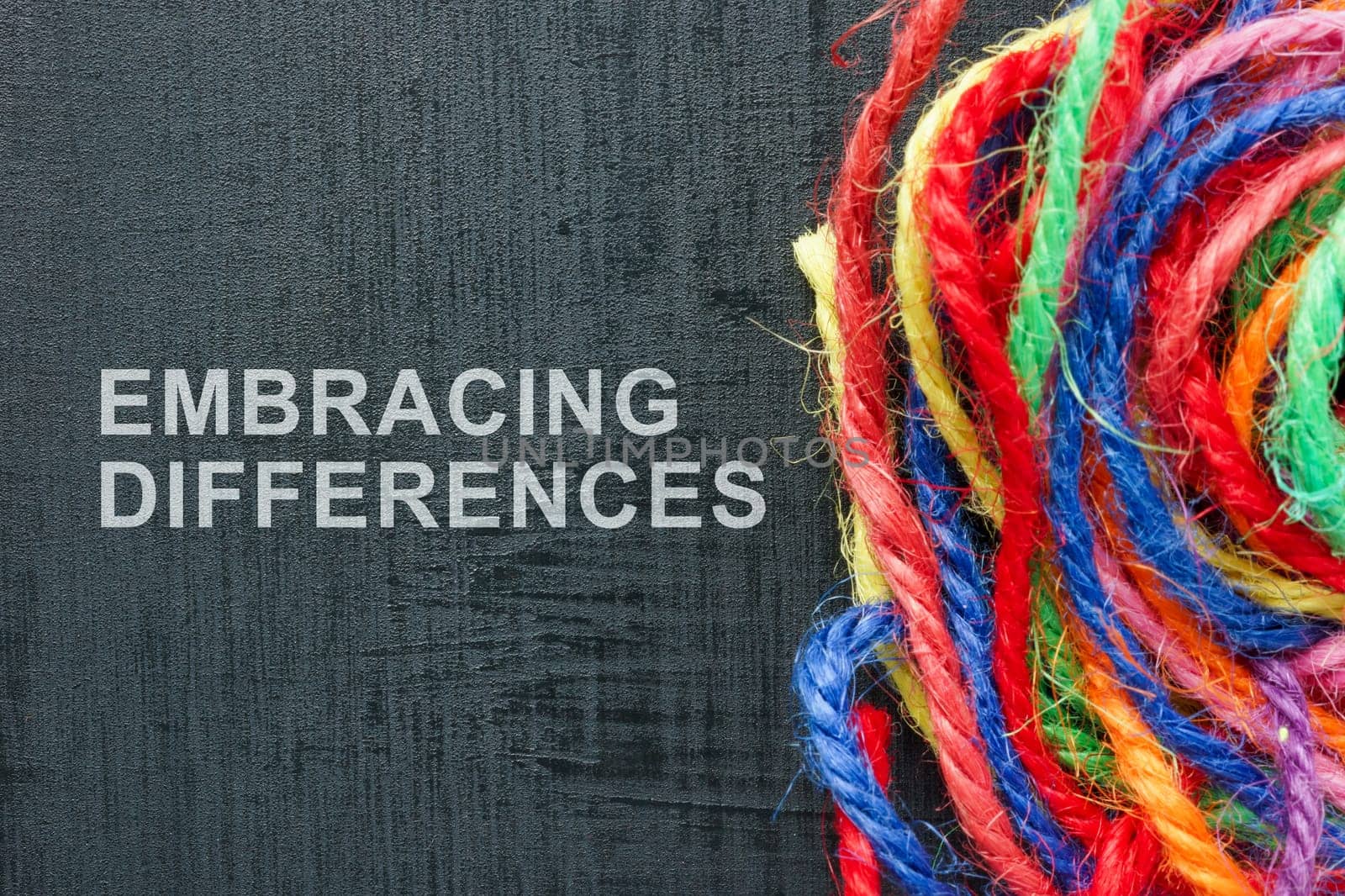 Words Embracing differences next to a ball of colored threads. by designer491