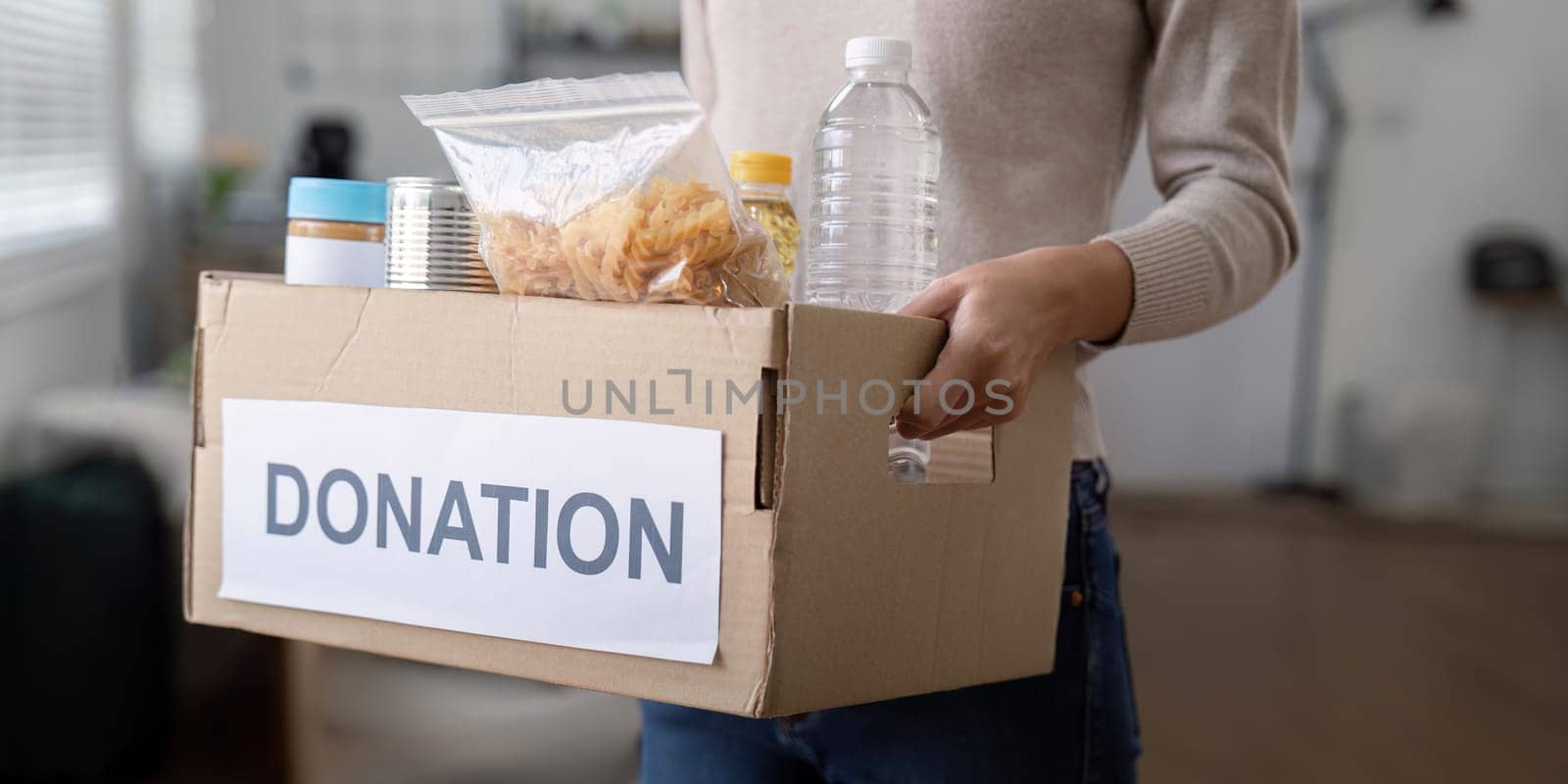 Woman volunteer holding food donation box at home by nateemee